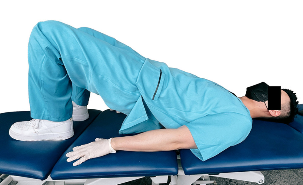 Demonstration of gluteal bridge exercise. The patient begins supine with the back flat against the table, then raises the back and hips to the elevated position shown.