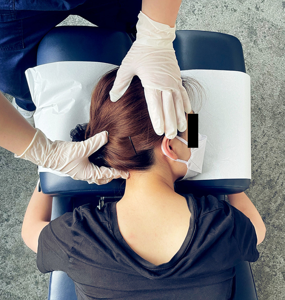 Cervical mobilization demonstration. The provider applies gentle posterior to anterior pressure to the left mid-cervical spine while the opposite hand ipsilaterally laterally flexes and slightly rotates the head and stabilizes it against the head rest. This procedure is repeated on the contralateral side as well as in the lower cervical and upper thoracic spine (not shown).