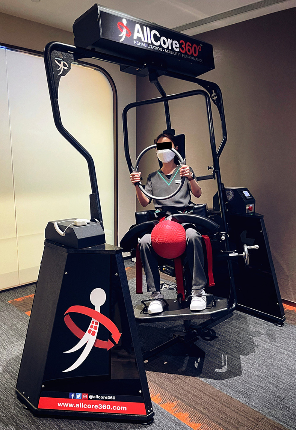 Core strengthening exercise demonstration. The patient sits in this device (Allcore360°, USA) that rotates slowly at different angles of inclination, while the patient isometrically contracts the core muscles to remain in the neutral, seated posture while holding a large ring in the hands and ball between the knees.