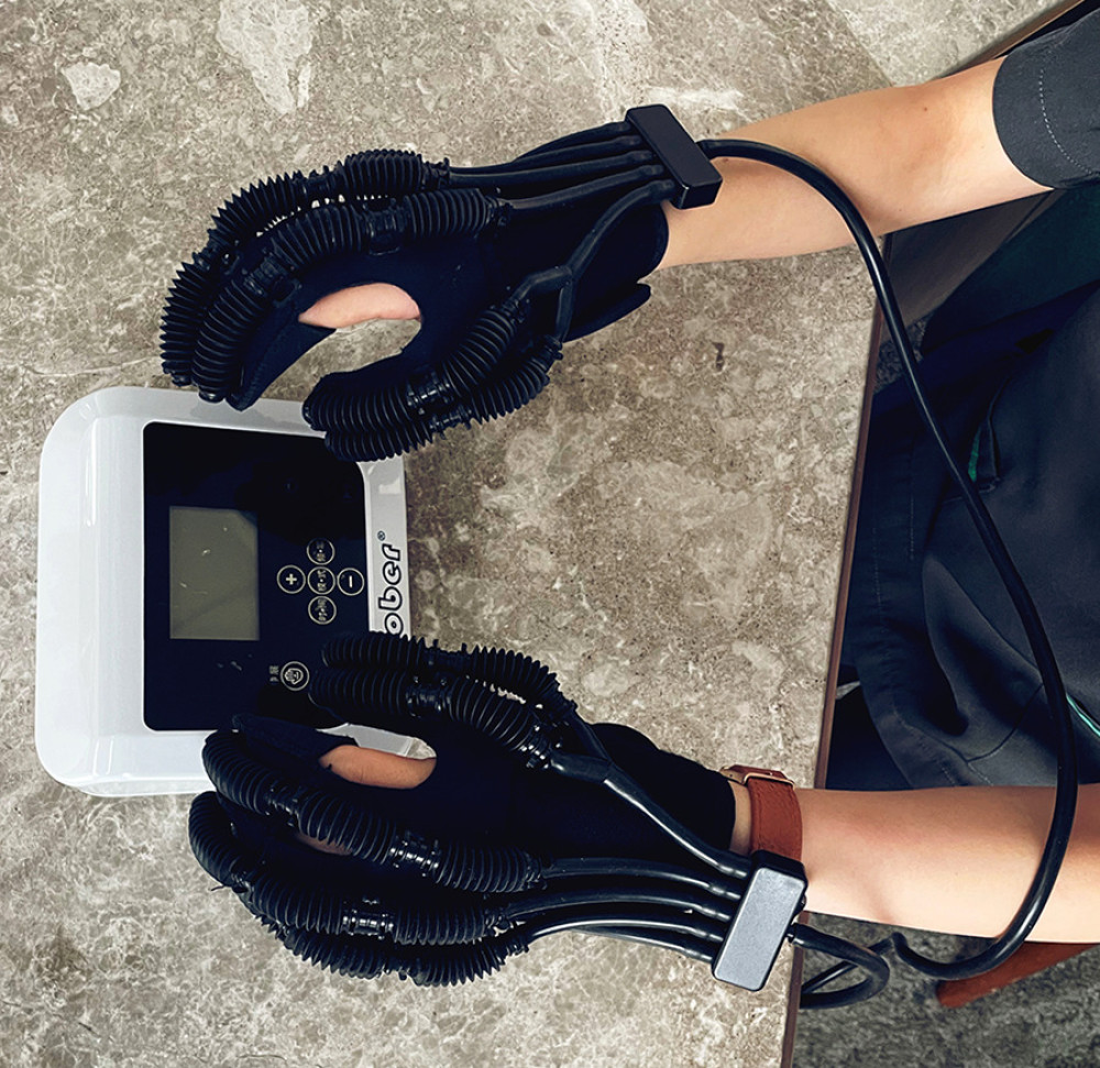Hand strength rehabilitation demonstration. The patient is wearing robotic gloves (Ober, China) and conducts fine motor activities for up to 30 min per day. Also shown is the control console that allows the level of mechanical assistance to be altered. Image from EC.