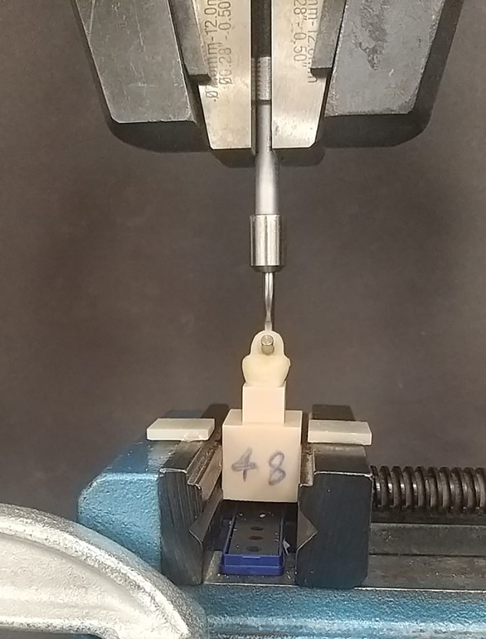 Universal testing machine showing engagement of the test samples for the pull-off test with handles of the provisional crowns aligned to engage the sample handle perpendicular to the line of direction of pulling force. Photograph taken using a digital single-lens reflex (DSLR) camera (Canon EOS 700D) with 100 mm macro lens) with/without ring flash.